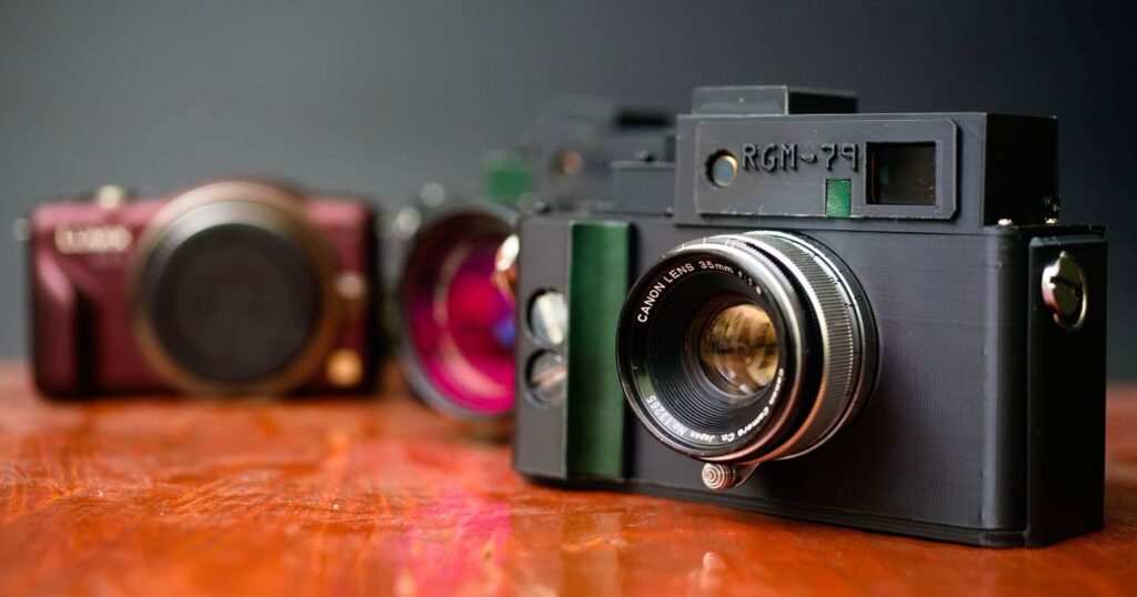 DIY Project Turns a Panasonic GF3 and Soviet Fed 5 Into a Digital Rangefinder Three vintage cameras are displayed on a wooden surface, with one black camera in sharp focus in the foreground and two blurred cameras in the background against a dark backdrop.