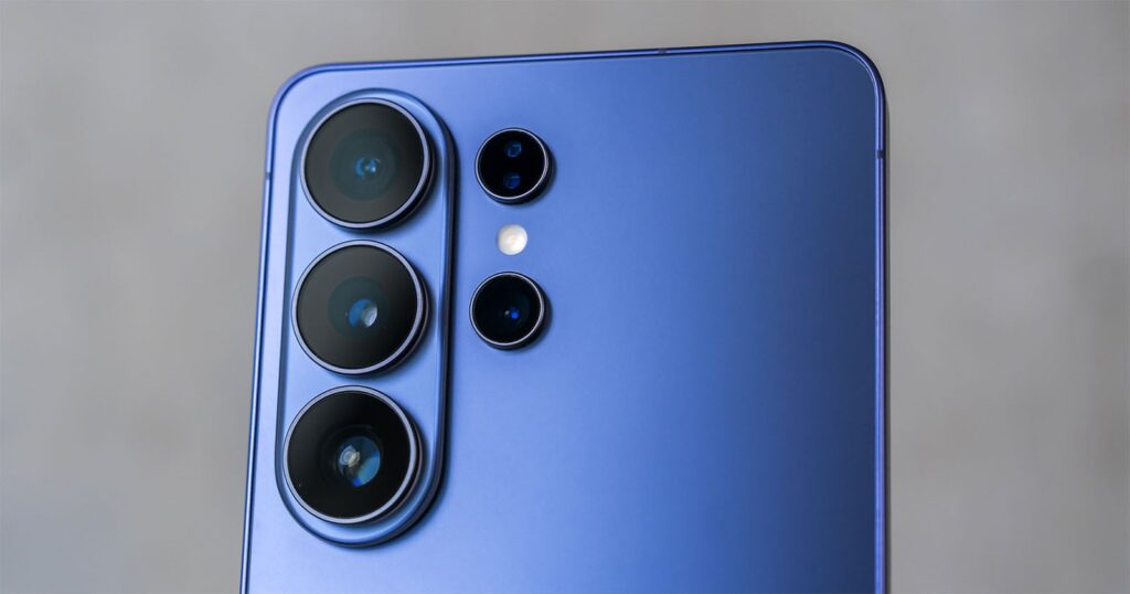 Samsung’s Competitors Have a Better Samsung Camera Than Samsung Does Close-up of the rear camera module of a blue smartphone with four camera lenses and a flash, set against a blurred gray background.
