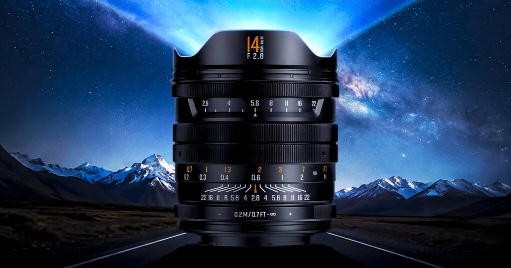 Brightin Star’s New 14mm f/2.8 Lens Promises High-End Astro Photos A wide-angle camera lens stands upright on a road, with snow-capped mountains and a starry night sky in the background, creating a dramatic and futuristic effect.