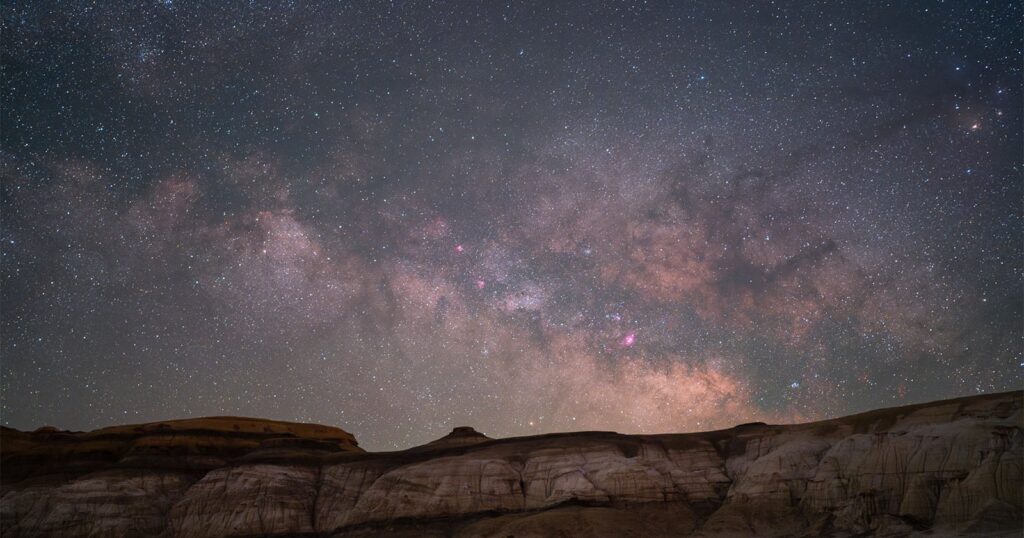Photographer’s New App Takes the Guesswork Out of Milky Way Photography A star-filled night sky with the Milky Way galaxy glowing above rugged, rocky cliffs in the foreground. The scene highlights bright stars, cosmic dust, and soft, colorful nebulae stretching across the horizon.