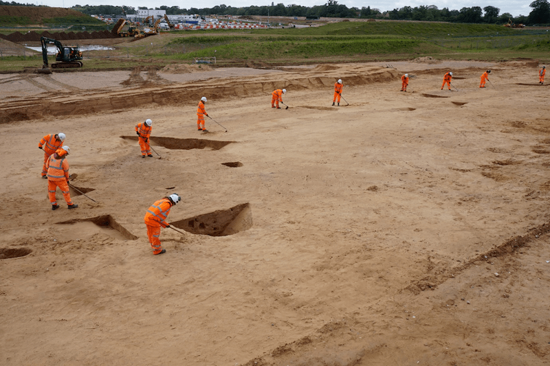 British Archeologists Find 5800-Year-Old Neolithic Monument in Suffolk Oxford Cotswold Archaeology field archaeologists excavating the long enclosure using tools such as shovels, wheelbarrows and hoes