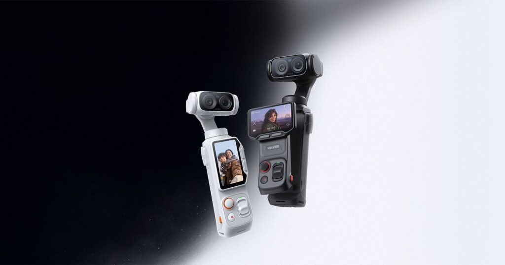 Insta360 CEO’s Dream Camera Is One You Won’t Even Think About At All Two handheld camera gimbals, one white and one black, each with dual lenses and a small built-in screen displaying people. The devices are shown against a black-to-white gradient background.