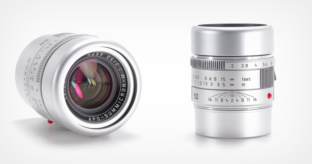 Two silver camera lenses are shown: one standing upright displaying its focus and aperture markings, the other lying on its side, showing its glass element and lens branding "APO-SUMMICRON-M 1:2/50.