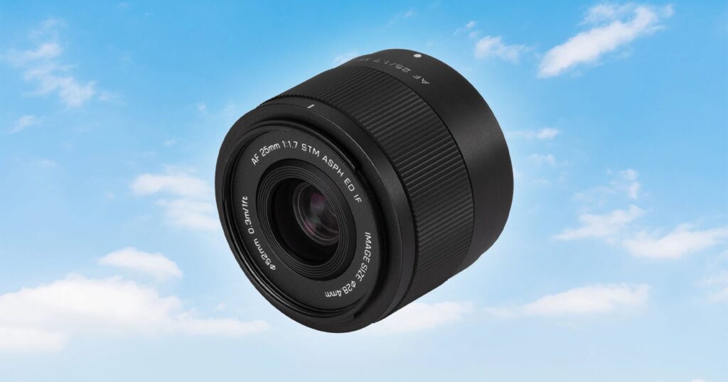 Viltrox Is Gearing Up for a Micro Four Thirds Reveal A black camera lens floating against a bright blue sky with scattered white clouds.
