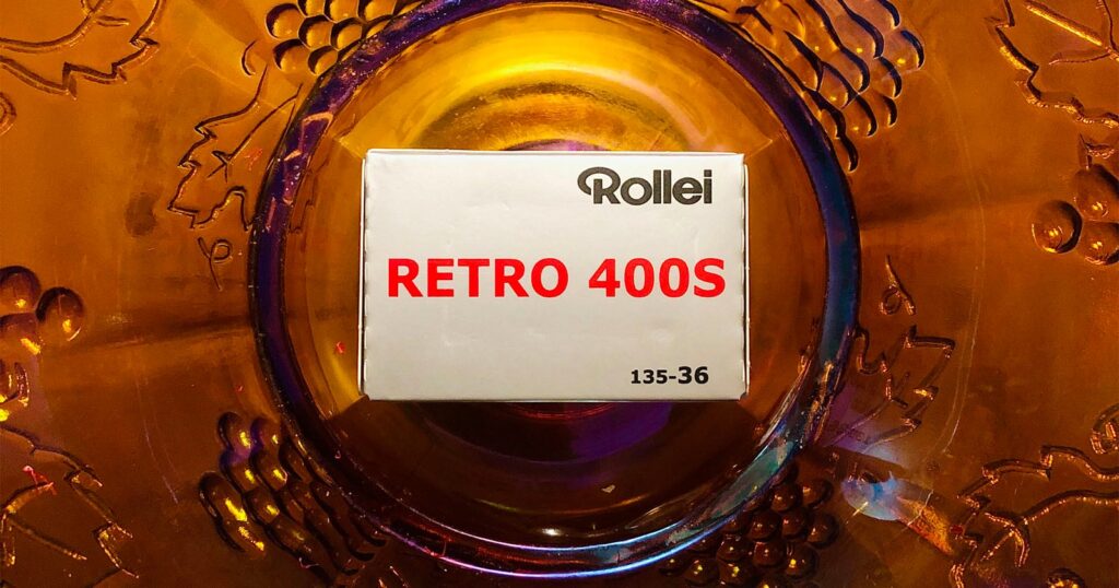 Rollei Retro 400S Is a Film for Making Loud, Brash, Dramatic Statements A box of Rollei Retro 400S 135-36 film sits centered on a decorative amber-colored glass plate.