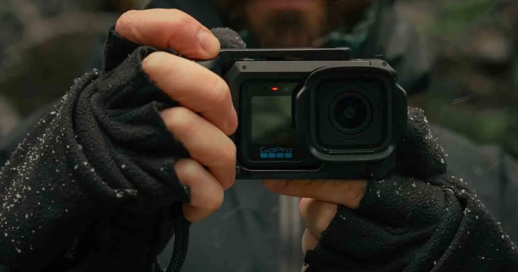 GoPro’s Founder Promises It Isn’t Done Making Consumer Cameras A person wearing black fingerless gloves holds a GoPro camera in a protective housing, with a small red light visible on the front.