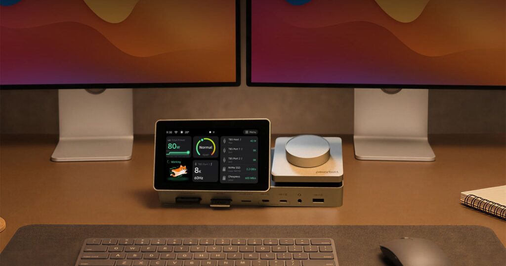 A desk setup featuring a central docking station with a digital display, flanked by two computer monitors, a keyboard, and a mouse.