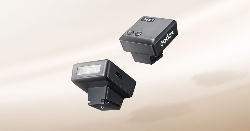 Godox’s $25 iM10 Mini Flash Is a Cute Little Fella Two black Godox iM10 compact flashes are shown against a light beige background, one displaying its front light panel and side USB-C port, and the other showing its top control buttons and battery indicator lights.