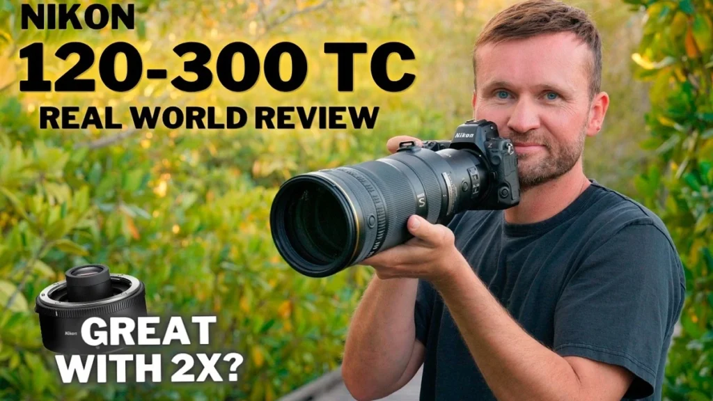 Nikon 120-300mm f/2.8 Review 2026: Worth the Size? Bearded man in a dark t-shirt raising a Nikon Z camera with a telephoto zoom lens outdoors among green foliage.