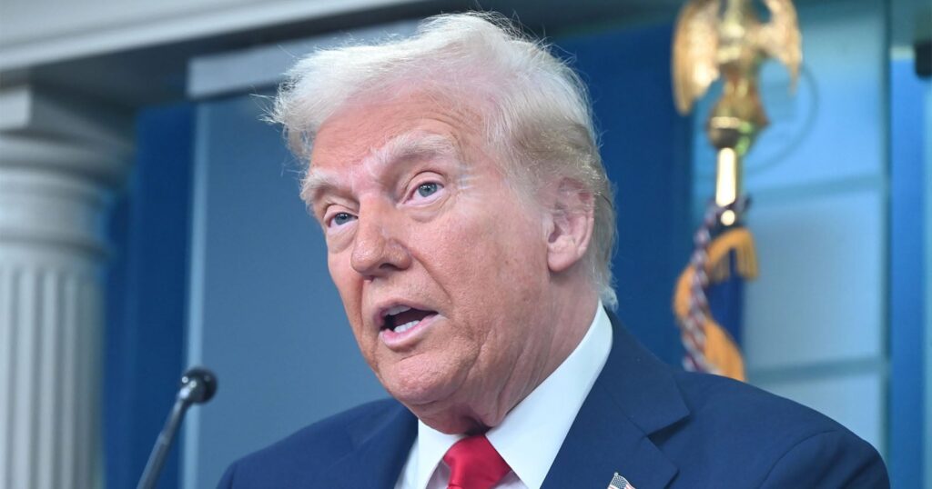 Trump Says He Will Ban the Term ‘Artificial Intelligence’ Donald Trump speaks at a podium with a blue background and a gold eagle emblem visible behind him.