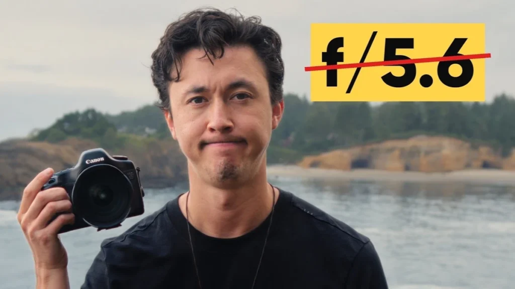 Man with wavy dark hair holding a Canon camera up to the lens, wearing a black shirt, with a yellow graphic reading f/5.6 crossed out in red.